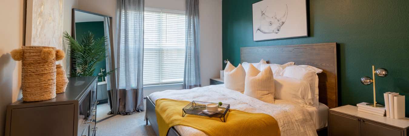 Stylish apartment bedroom with wood furniture and dark green wall behind bed.