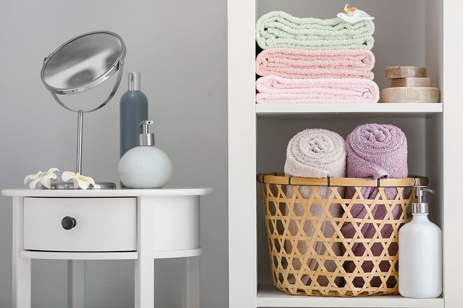 A shelf with colorful bath towels next to a small white table with a mirror on it